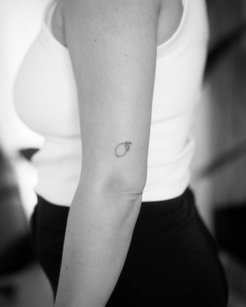 Minimalistic style lemon tattoo located on the upper arm.