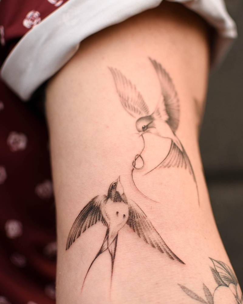 Illustrative style swallow couple tattoo located on the bicep.