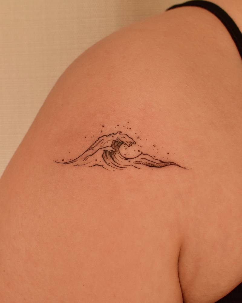 Little wave tattoo in illustrative style located on the shoulder.