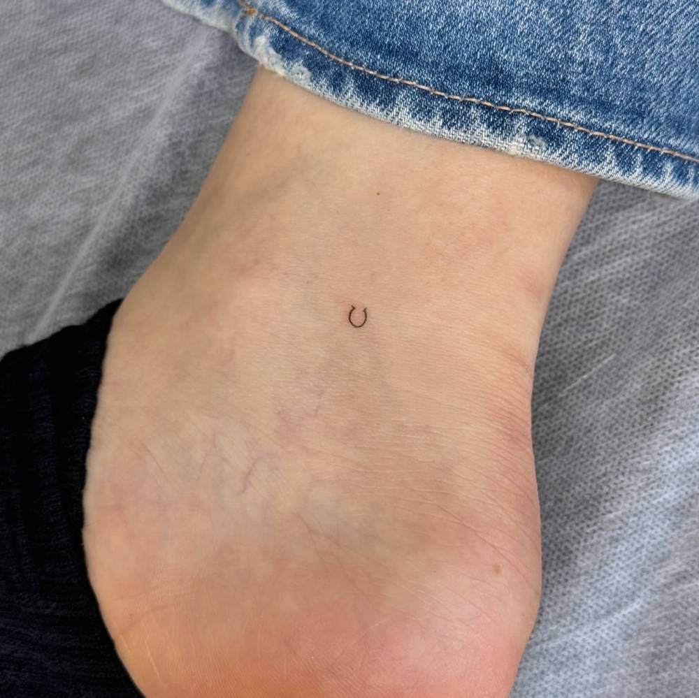 Tiny minimalistic horseshoe tattoo located on the ankle.