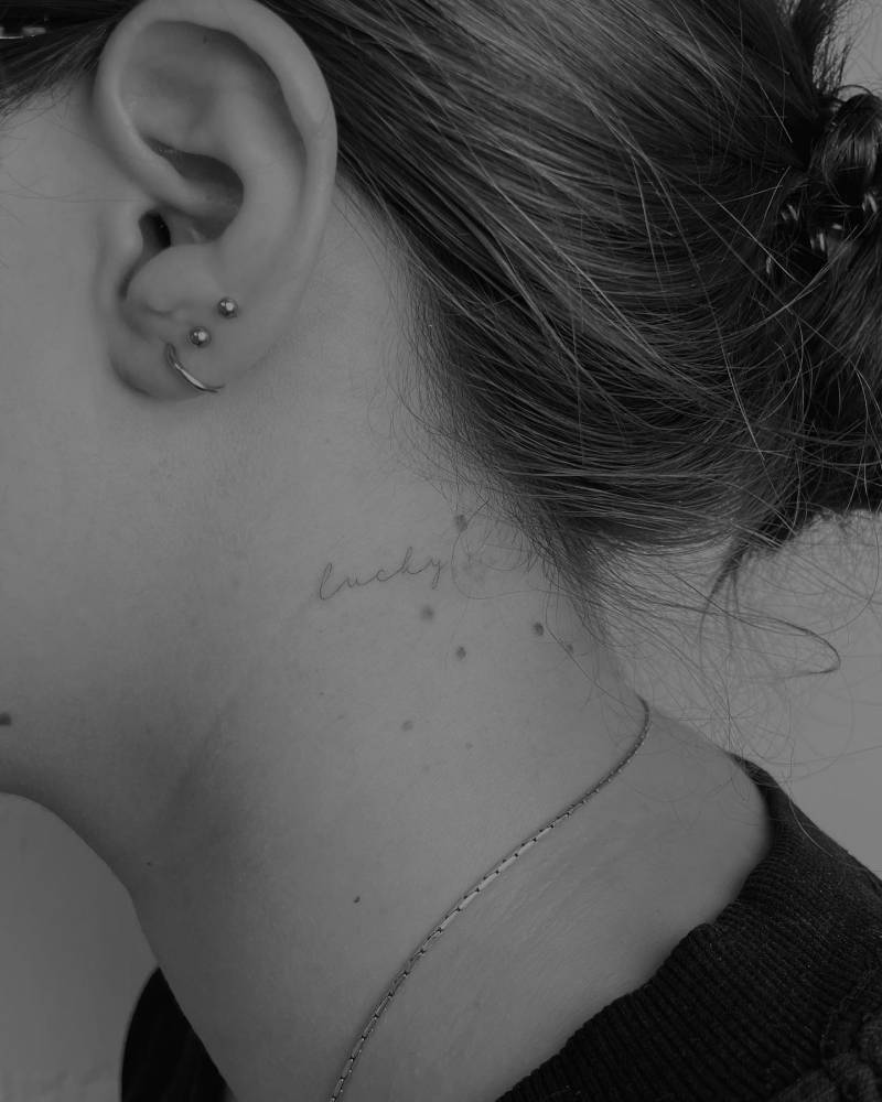 Tattoo of the word "lucky" located on the neck.