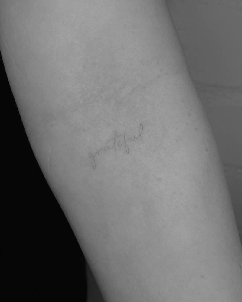 Tattoo of the word "grateful" handwritten on the inner forearm.