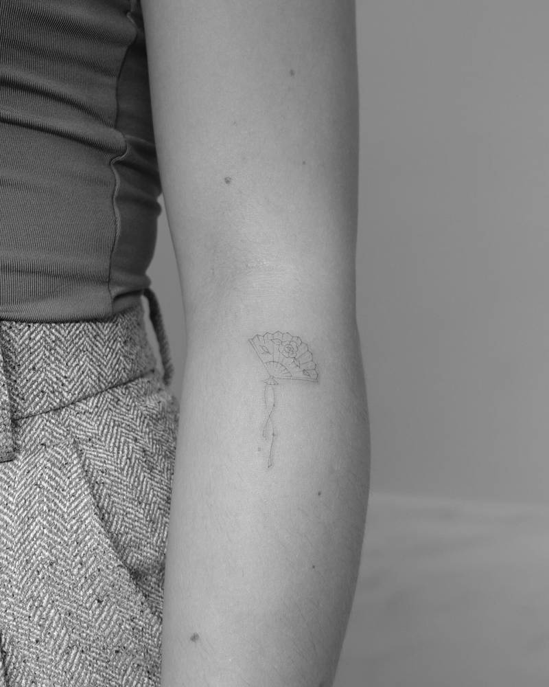 Hand fan tattoo in fine line style located on the forearm.