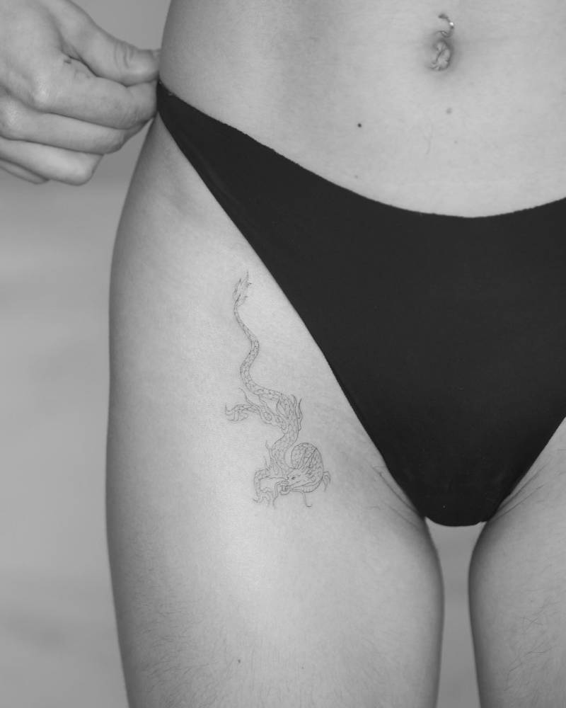 Fine line style dragon tattoo placed on the pelvis.