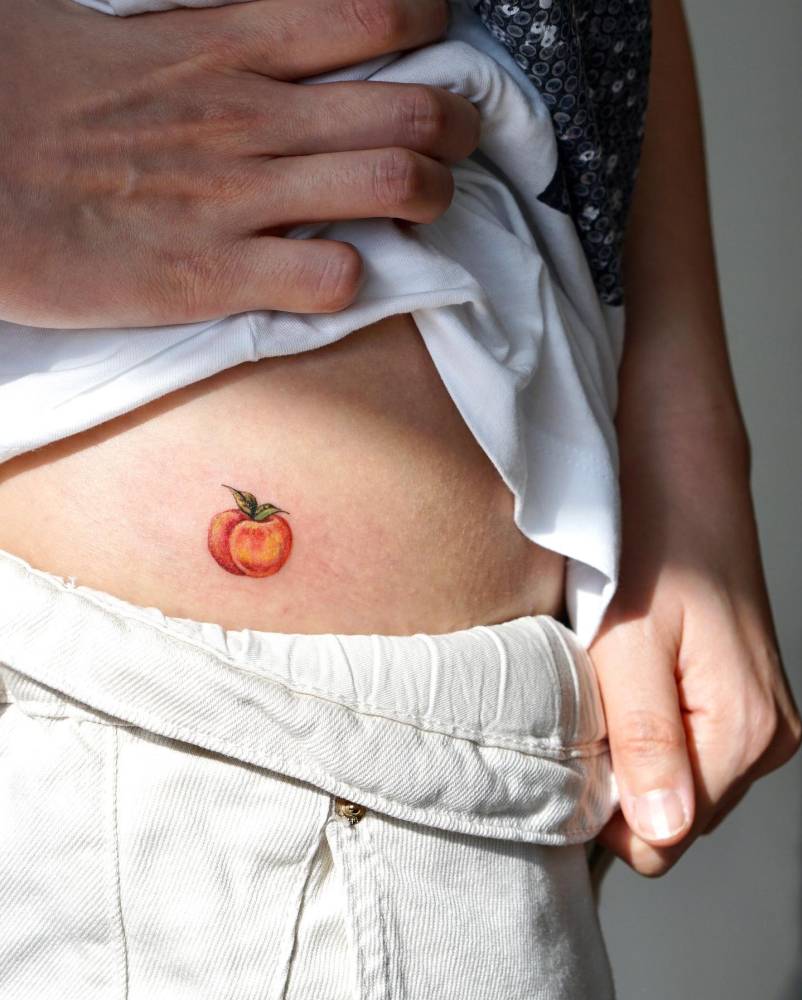 Tiny watercolor style peach tattoo located on the hip.