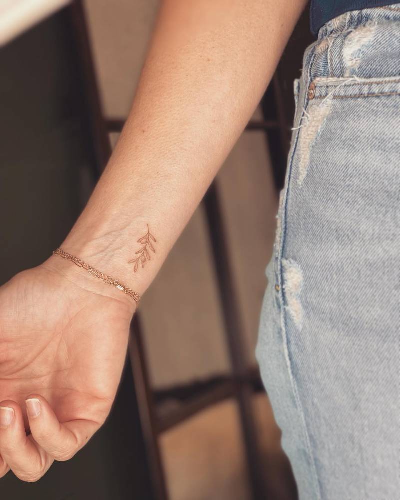 Fine line style olive branch tattoo located on the wrist.