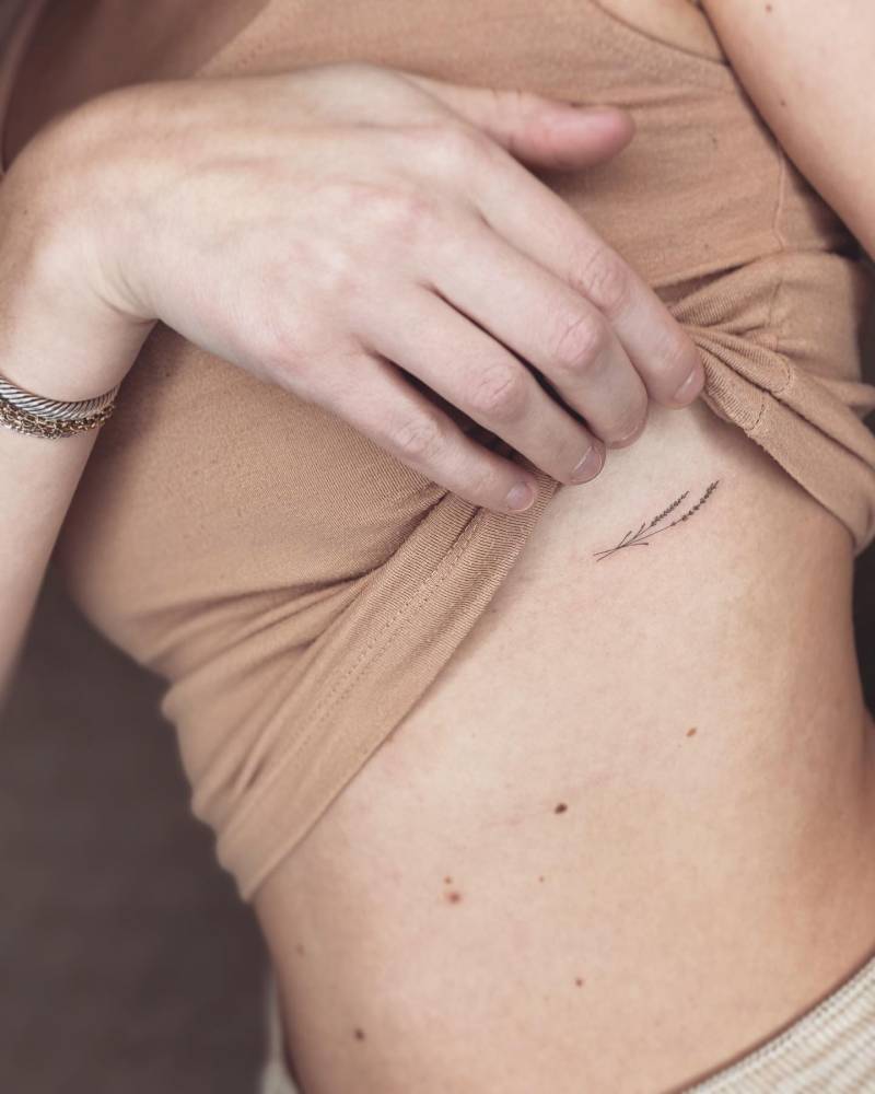 Fine line style lavender tattoo located on the rib.