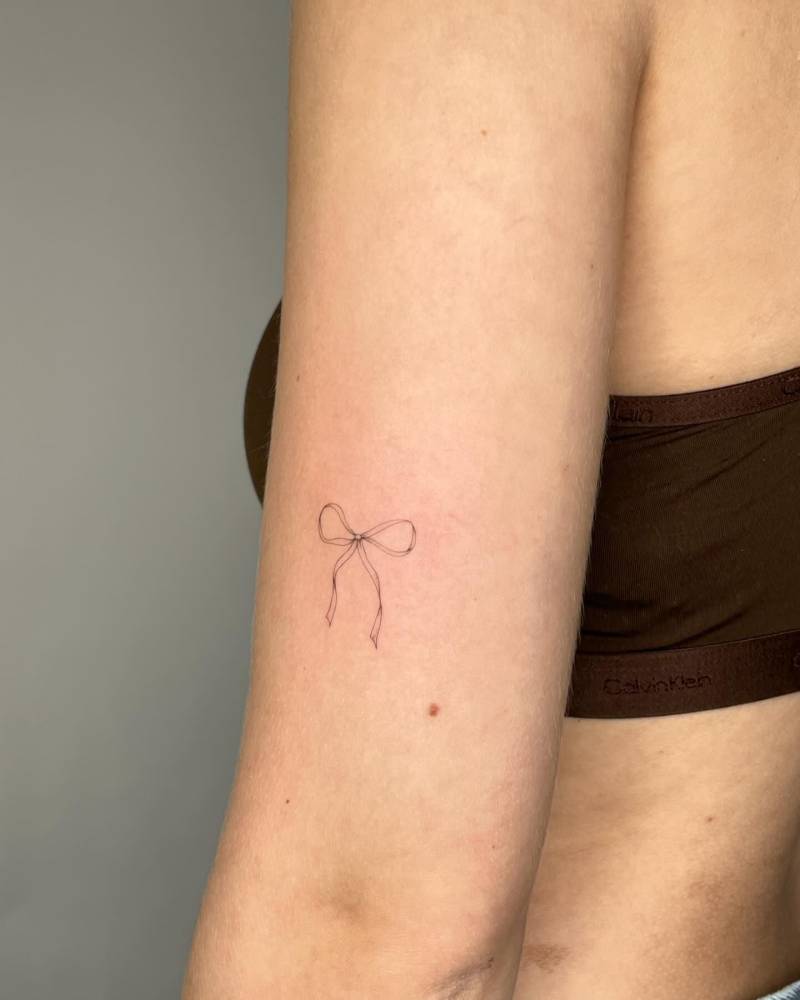 Fine line style ribbon tattoo located on the upper arm.