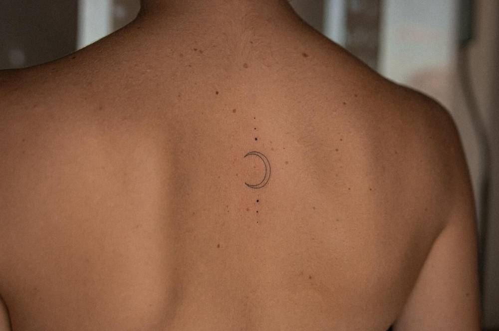 Minimalistic style crescent moon tattoo located on the upper back.
