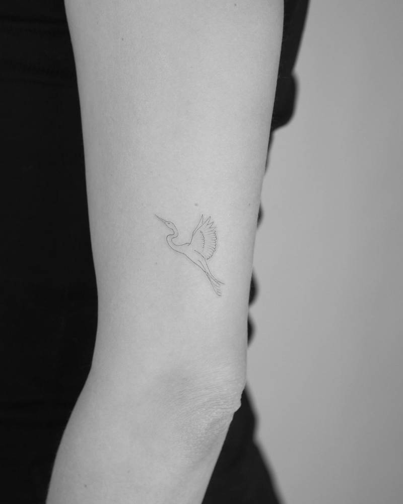 Fine line style crane tattoo located on the upper arm.