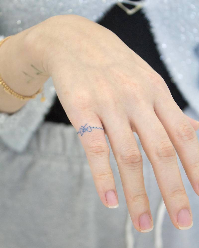 Minimalistic style blue bow ring tattooed on the finger.