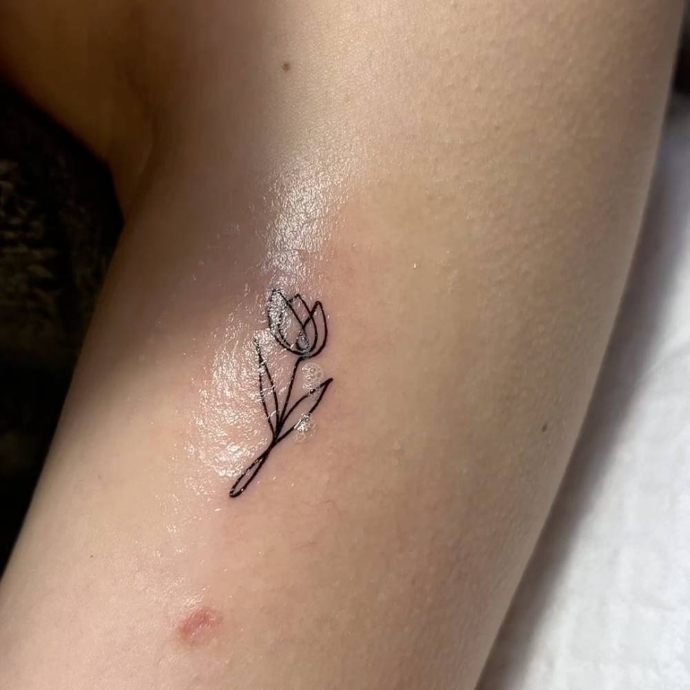 One line tulip tattoo placed on the upper arm, minimalistic style.