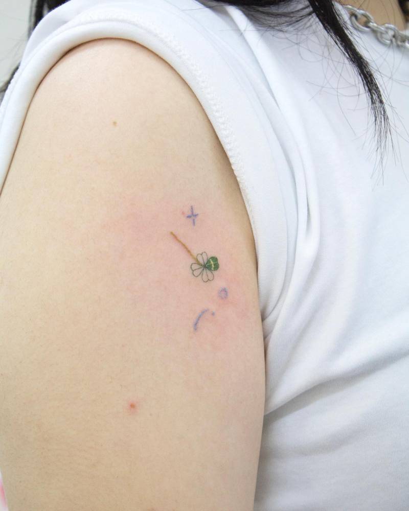 Four leaf clover tattoo in watercolor style located on the upper arm.