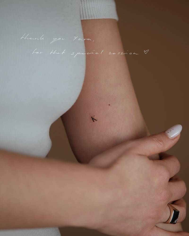 Tiny minimalistic letter "K" tattoo placed on the inner arm.
