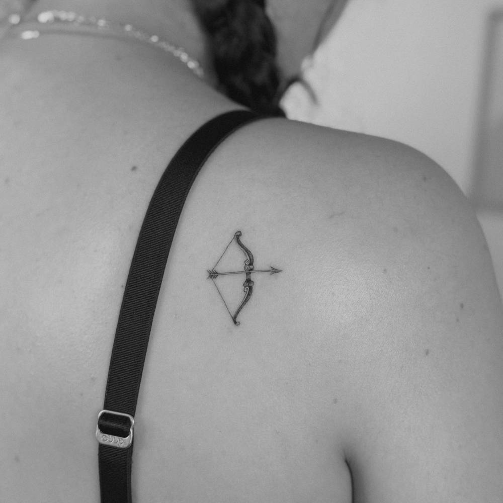 Illustrative style bow and arrow tattoo placed on the shoulder blade.