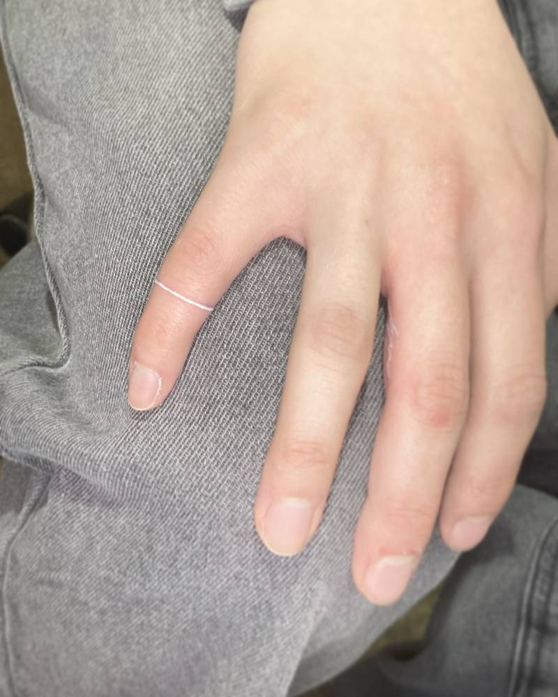 Minimalistic style white ring tattoo located on the finger.