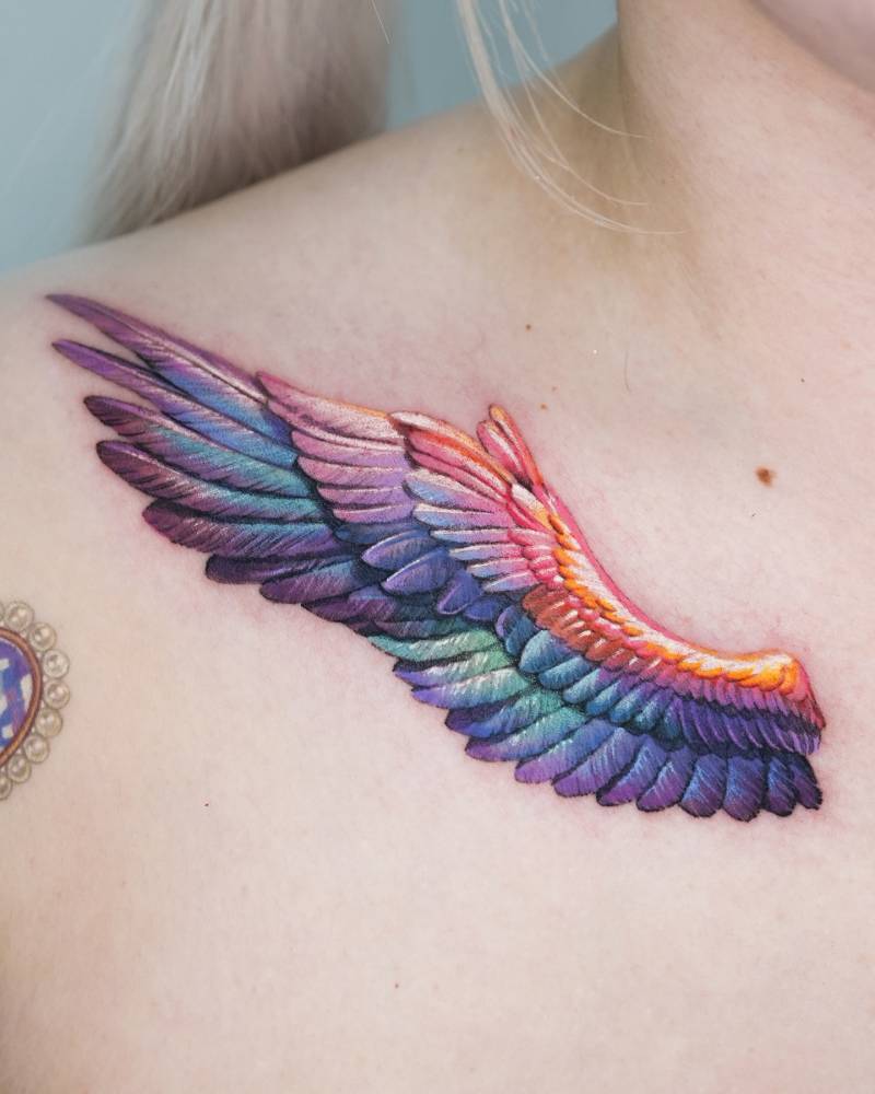 Realistic style wing tattoo located on the collarbone.