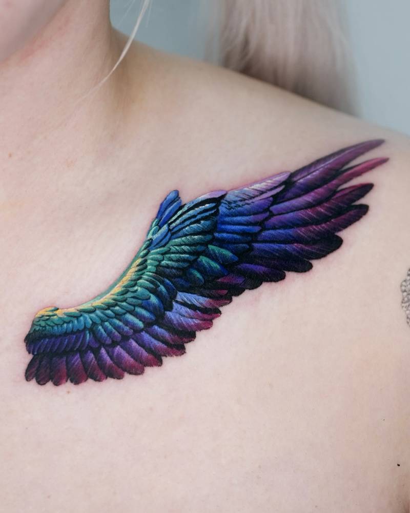 Realistic style wing tattoo located on the collarbone.
