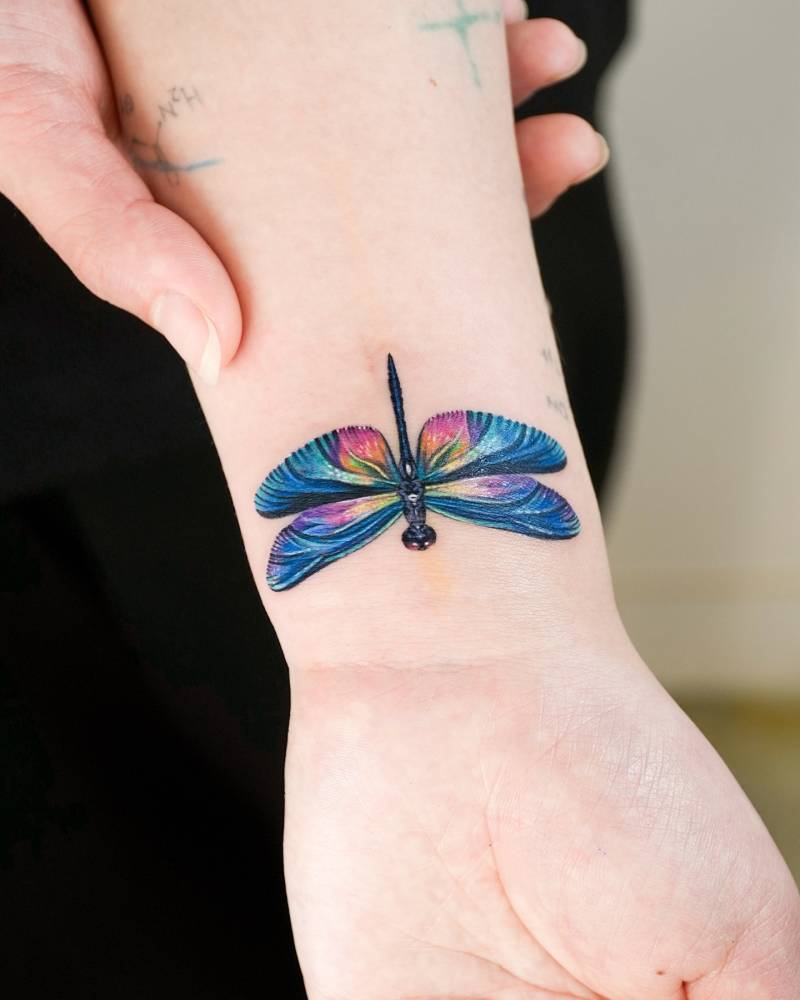 Realistic style dragonfly tattoo located on the wrist.