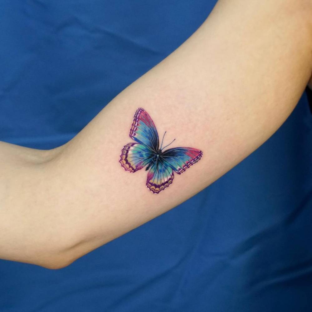 Blue butterfly tattoo located on the inner arm, realistic style.