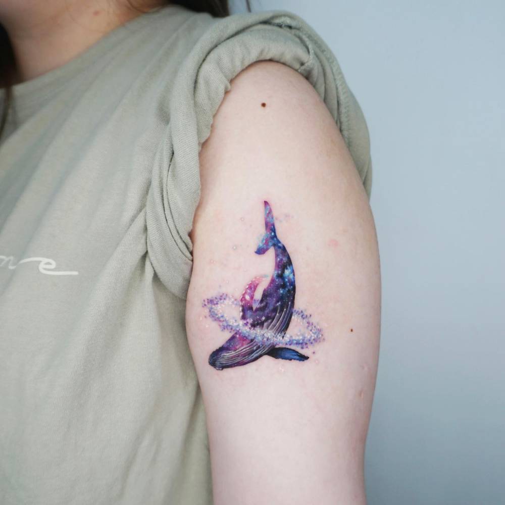 Space whale tattoo located on the upper arm, illustrative style.