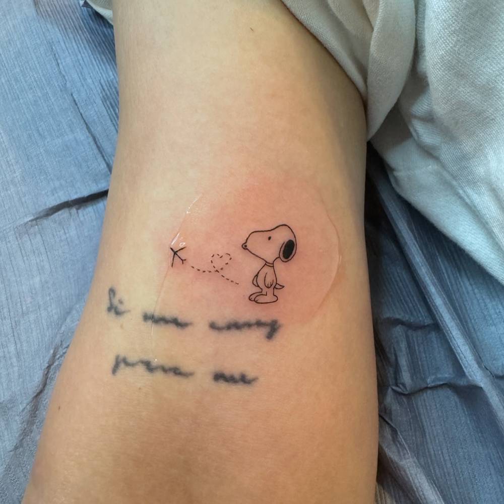 Cartoon style Snoopy and airplane tattoo located on the bicep.