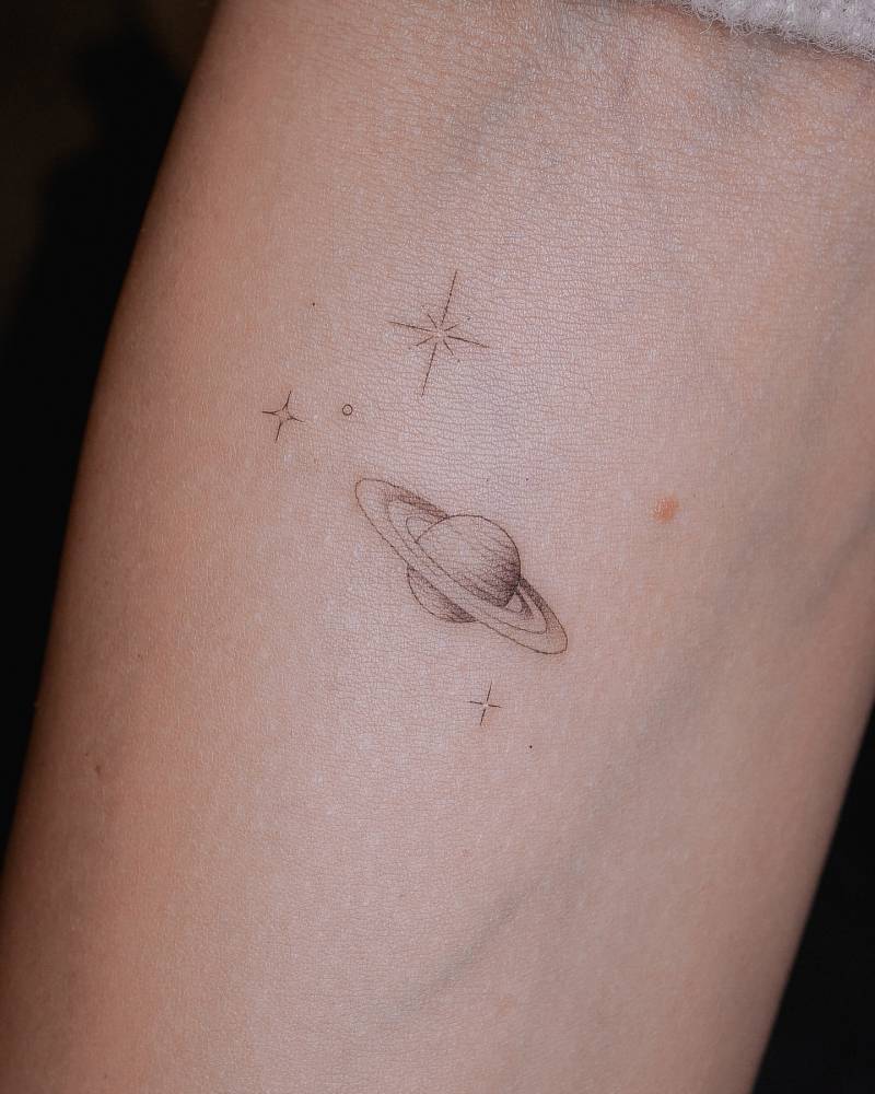 Saturn and sparkling stars tattoo located on the inner forearm, fine line style.