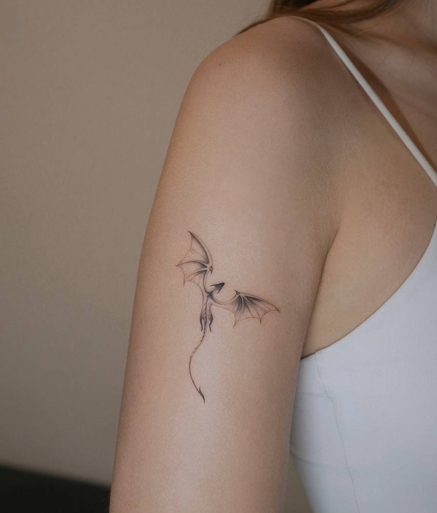Dragon tattoo in illustrative style located on the upper arm.