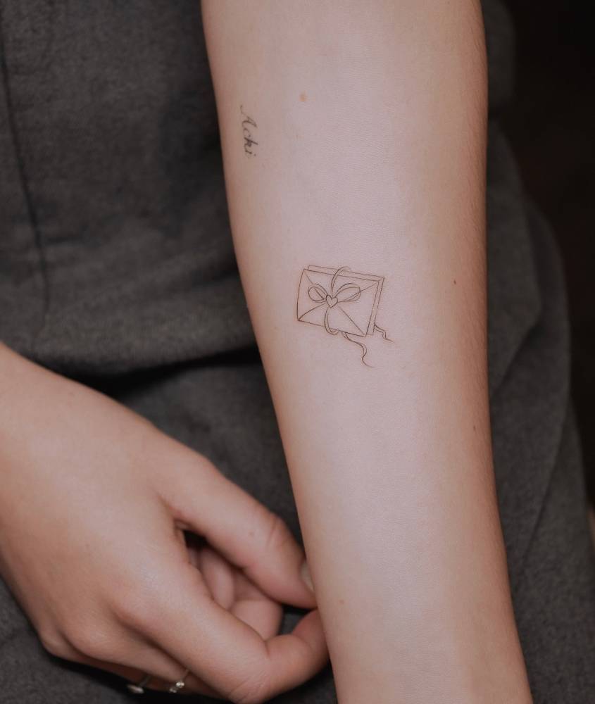 Love letter tattoo in fine line style located on the inner forearm.