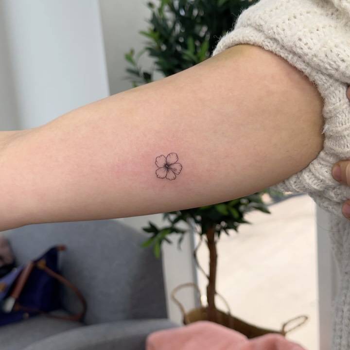 Fine line style tiny hibiscus flower tattoo located on the inner arm.