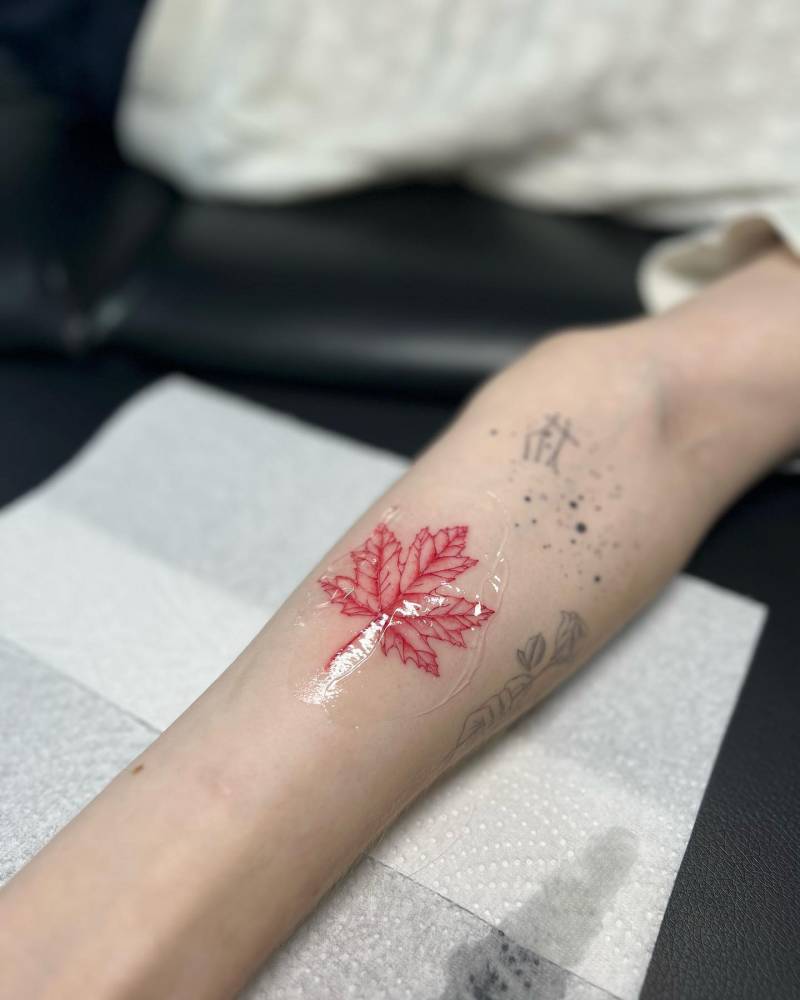 Red maple leaf tattoo located on the inner forearm.