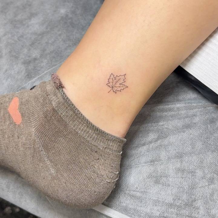 Fine line style maple leaf tattoo located on the ankle.