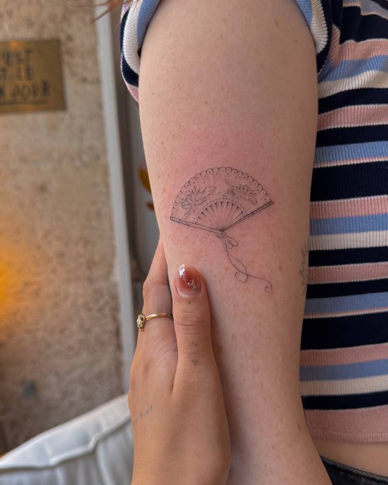 Fine line style hand fan tattoo located on the upper arm.