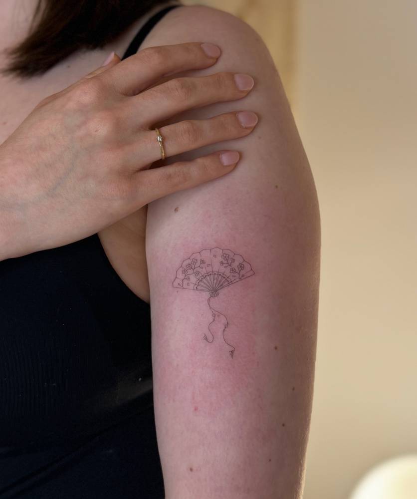 Fine line style hand fan tattoo done on the upper arm.