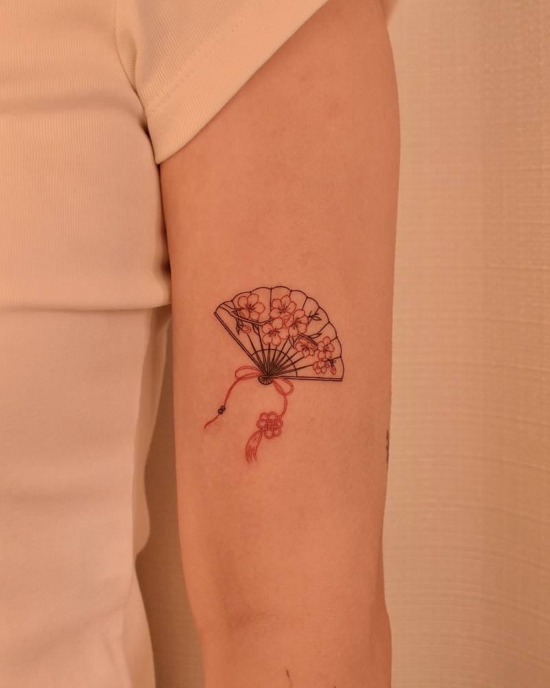 Cherry blossom hand fan tattoo in fine line style placed on the upper arm.