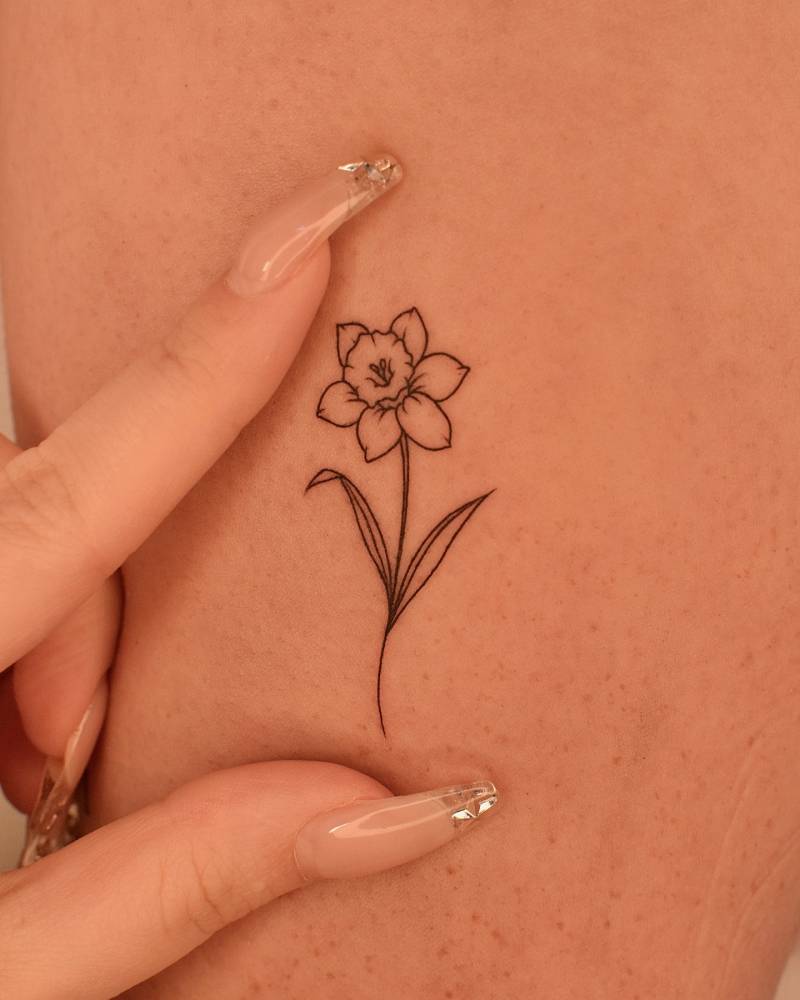 Fine line style narcissus flower tattooed on the upper arm.