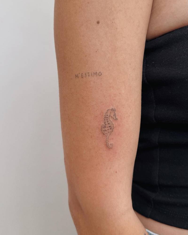 "M'estimo" and seahorse tattoos located on the upper arm.