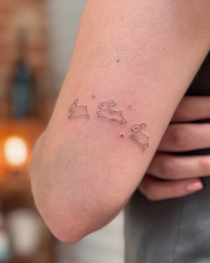Fine line style jumping rabbit tattoo located on the tricep.