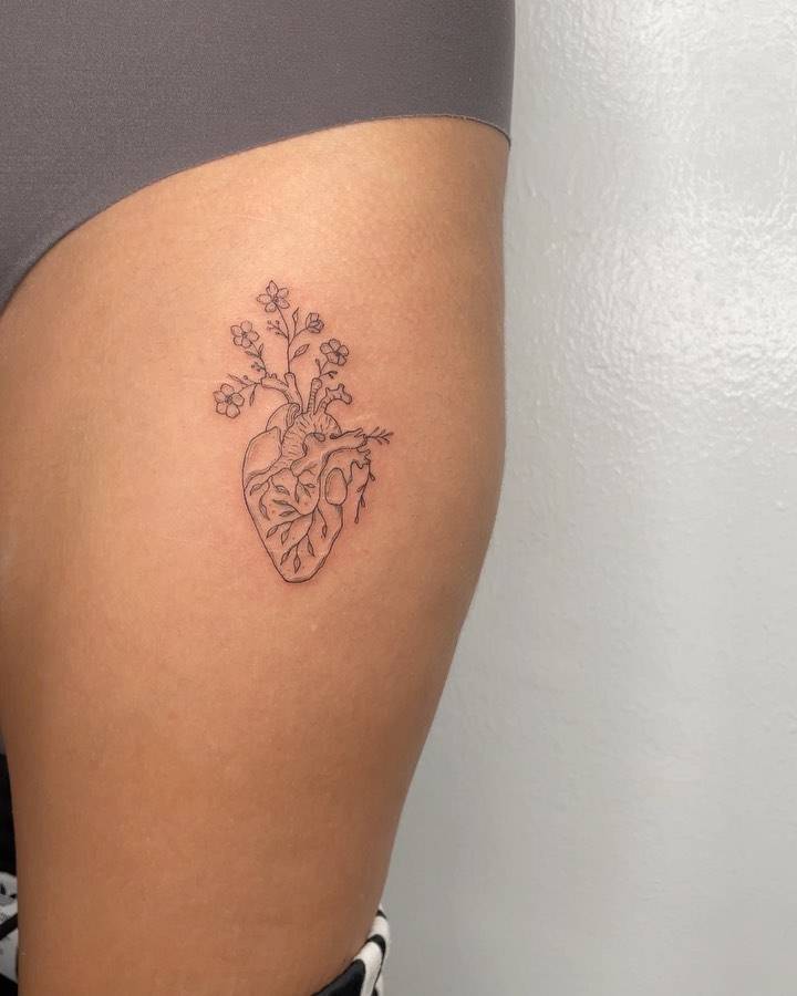 Anatomical heart and flowers tattooed on the thigh.