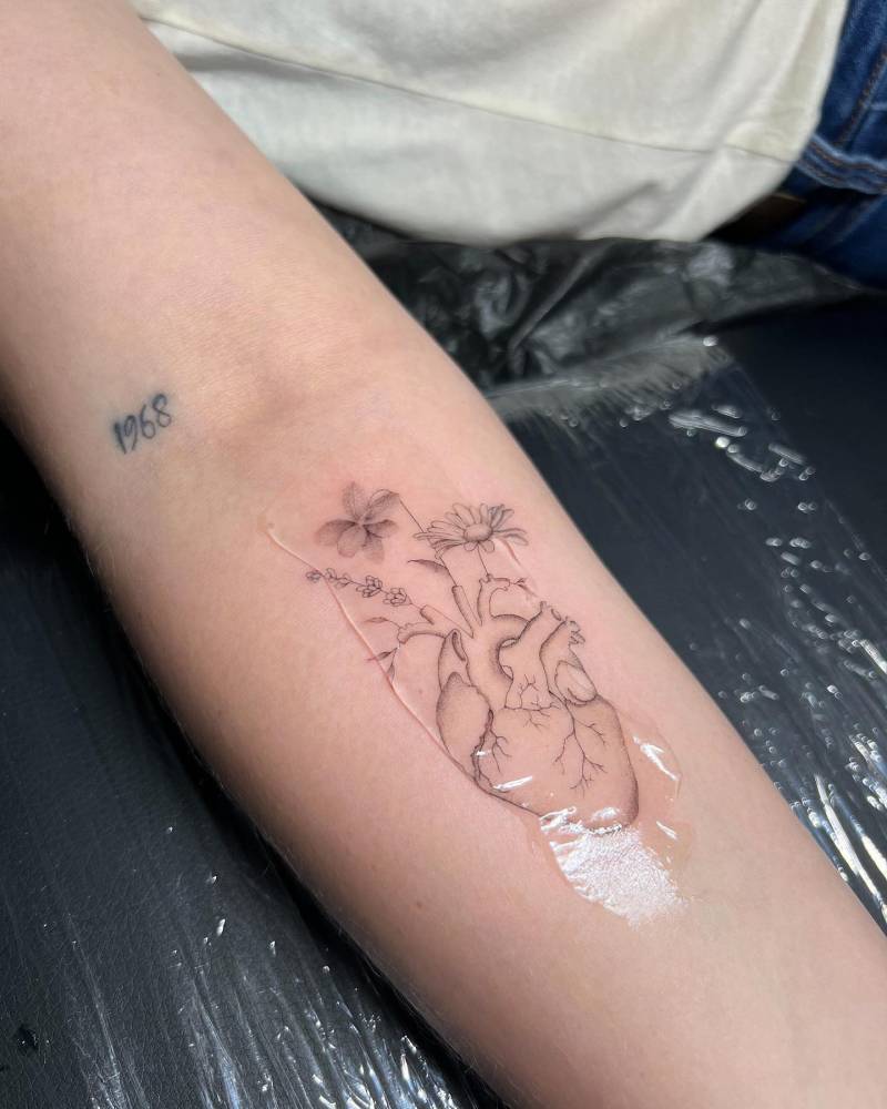 Single needle anatomical heart with flowers tattooed on the inner forearm.