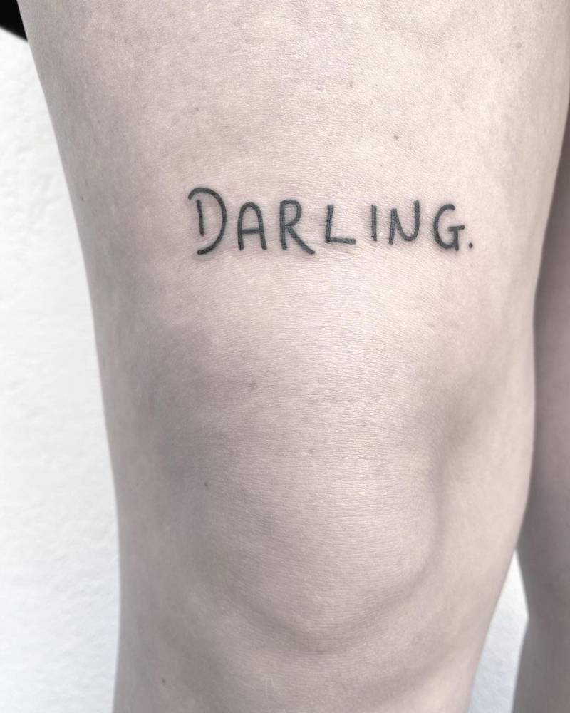 "Darling" lettering tattoo on the thigh.