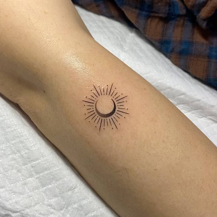 Minimalist sun and moon tattoo on the forearm.