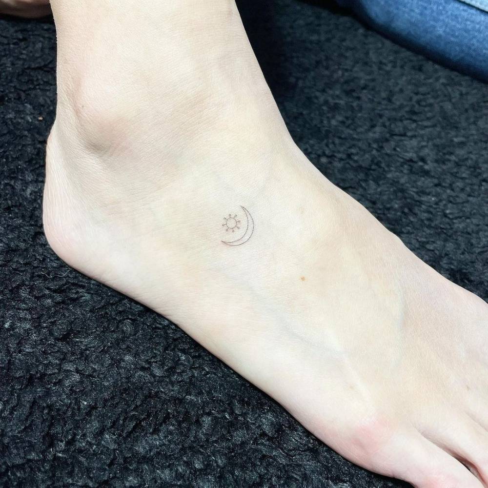 Minimalistic sun and moon tattoo located on the foot, done in fine line.