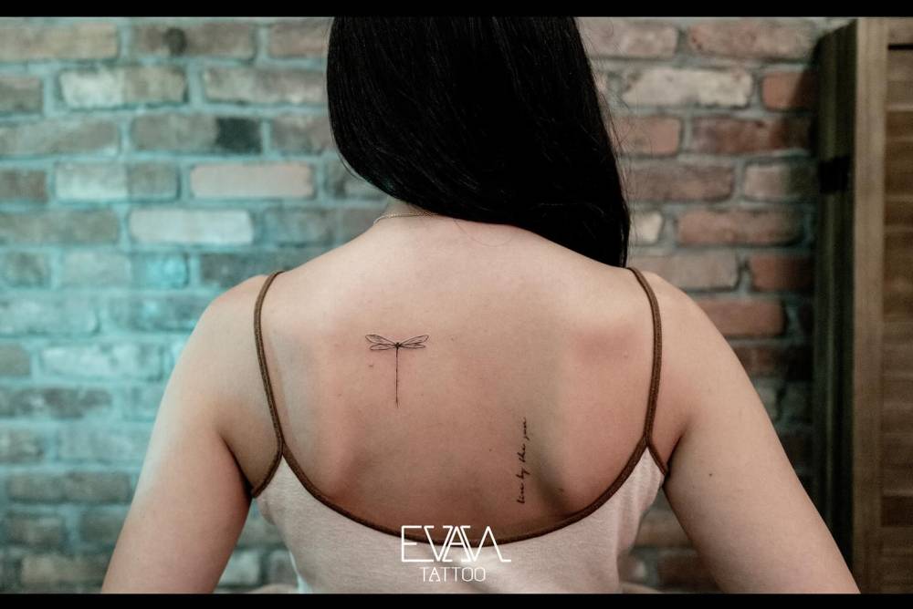 Dragonfly tattoo located on the upper back, minimalistic style.
