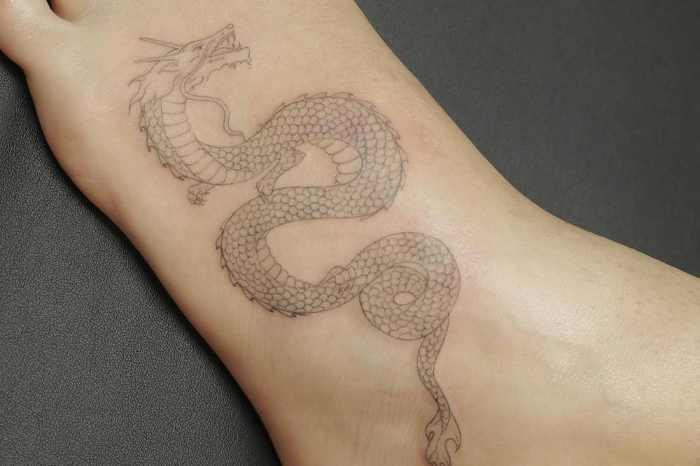 Fine line style dragon tattoo located on the foot.