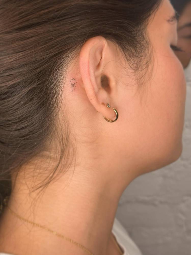 Tiny minimalistic jellyfish tattoo placed behind the ear.