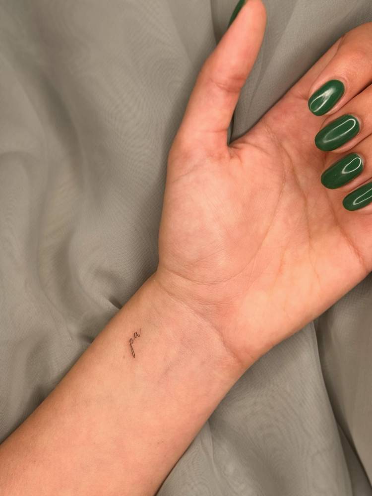 Tiny lettering tattoo of the word "pa" located on the wrist.