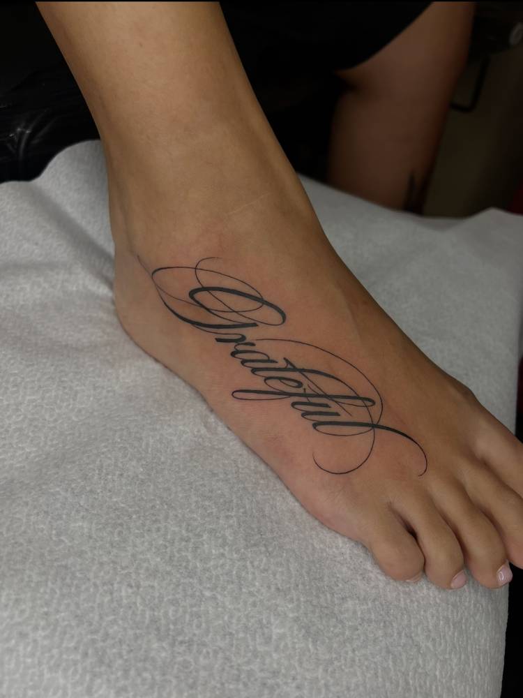 Word grateful in script font tattooed on the foot.