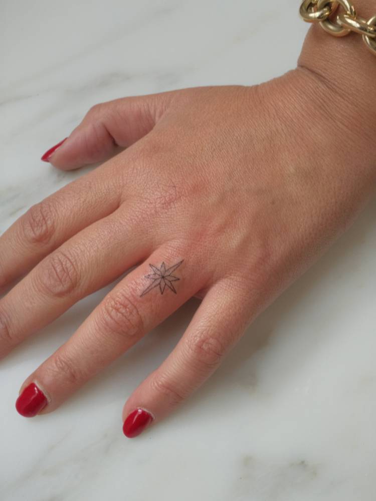 North star tattoo in fine line style located on the finger.