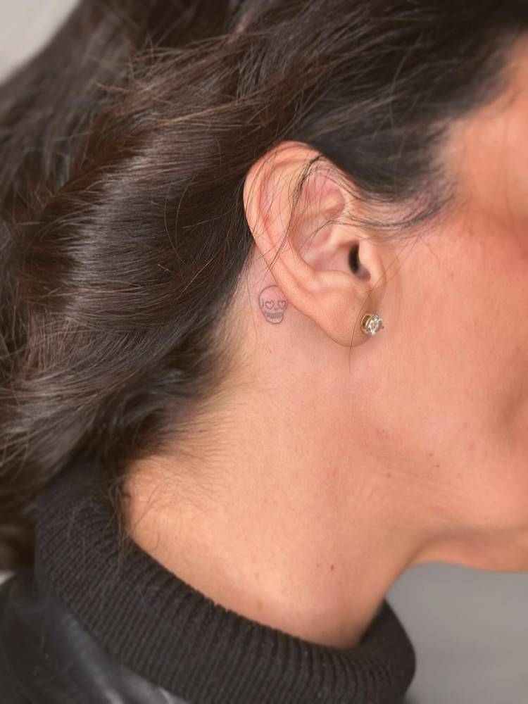 Fine line style tiny skull tattoo located behind the ear.
